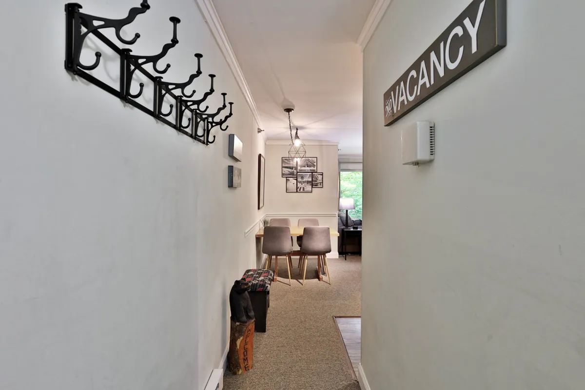 A view of the inviting entryway featuring a coat rack, a 'VACANCY' sign, and a glimpse into the dining area. The space is well-lit and welcoming, with stylish light fixtures and a sense of flow into the heart of the condo.