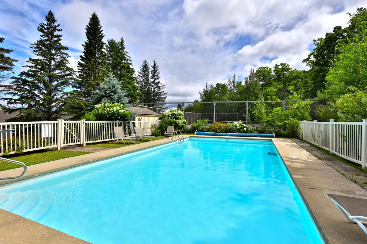 A beautifully maintained outdoor swimming pool surrounded by lush green foliage and a safety fence. Lounge chairs are set up along the poolside, inviting guests to relax in the sun or enjoy a refreshing swim. The space exudes a relaxed atmosphere, perfect for summer enjoyment and family-friendly gatherings.