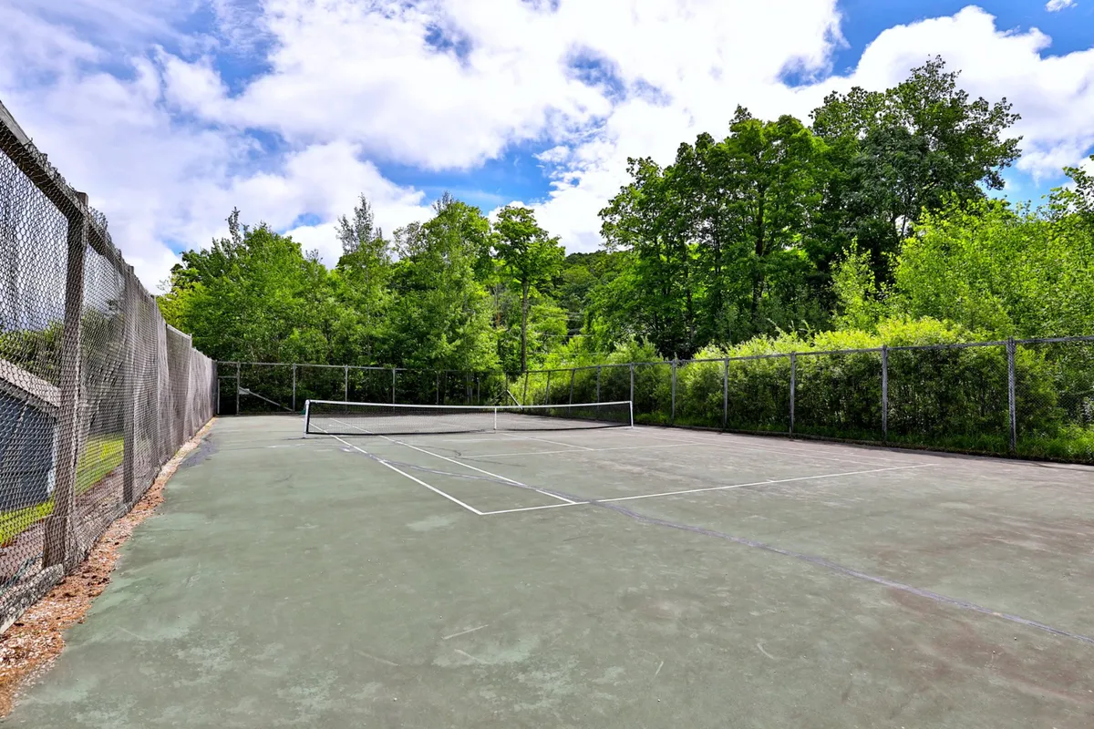 An energetic exterior image featuring a tennis court nestled among lush greenery. The scene exudes an active, recreational vibe, hinting at the variety of on-site or nearby sports and leisure options available to guests.