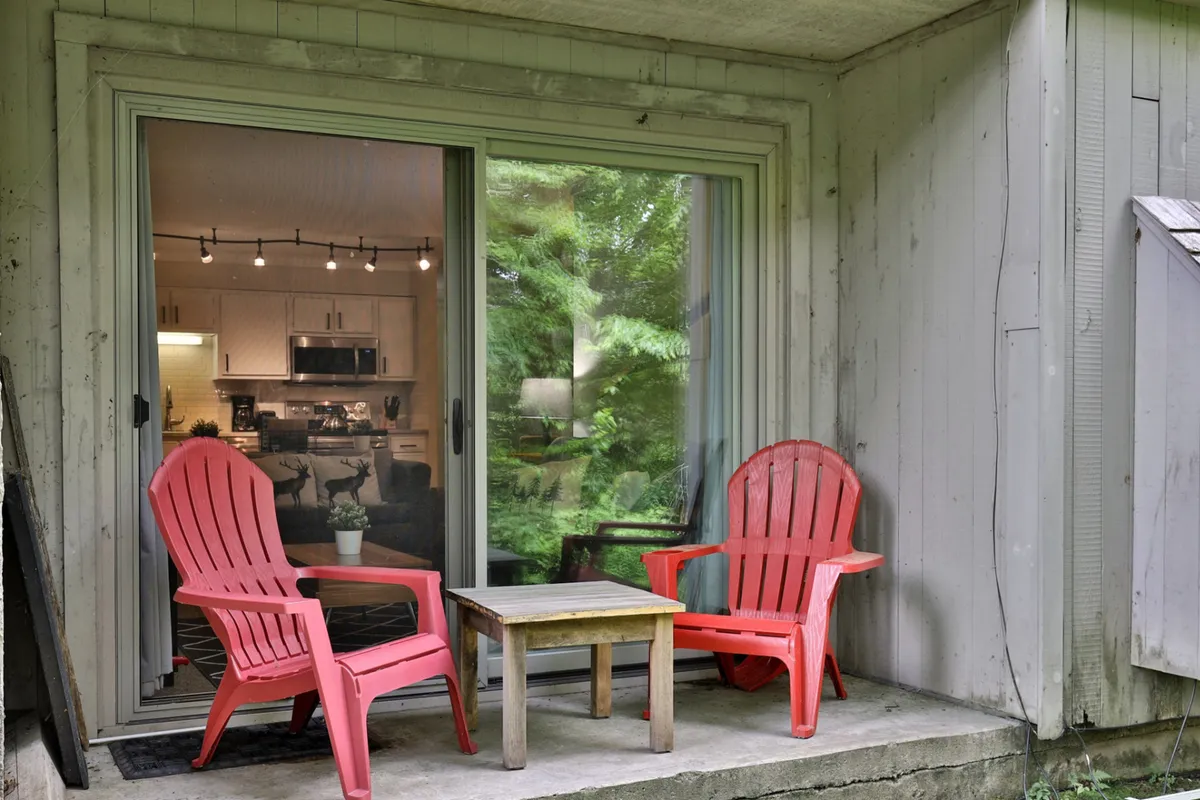 A cozy outdoor seating area with red Adirondack chairs and a small wooden table, set near a window and surrounded by greenery. The setting is intimate and inviting, perfect for relaxing at the start or end of an adventure-filled day.